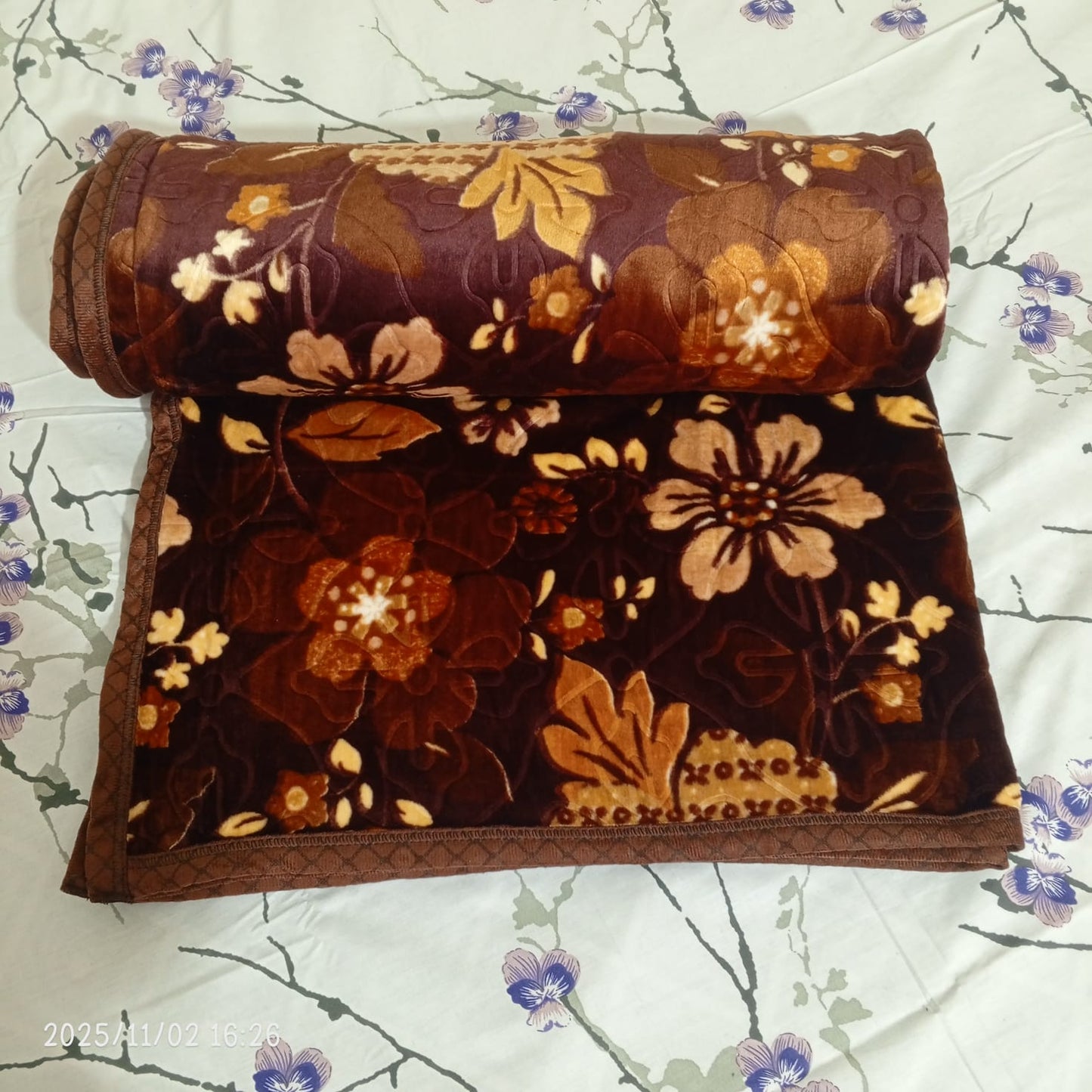 Brown floral blanket rolled on a floral bedsheet, cozy bedding decor