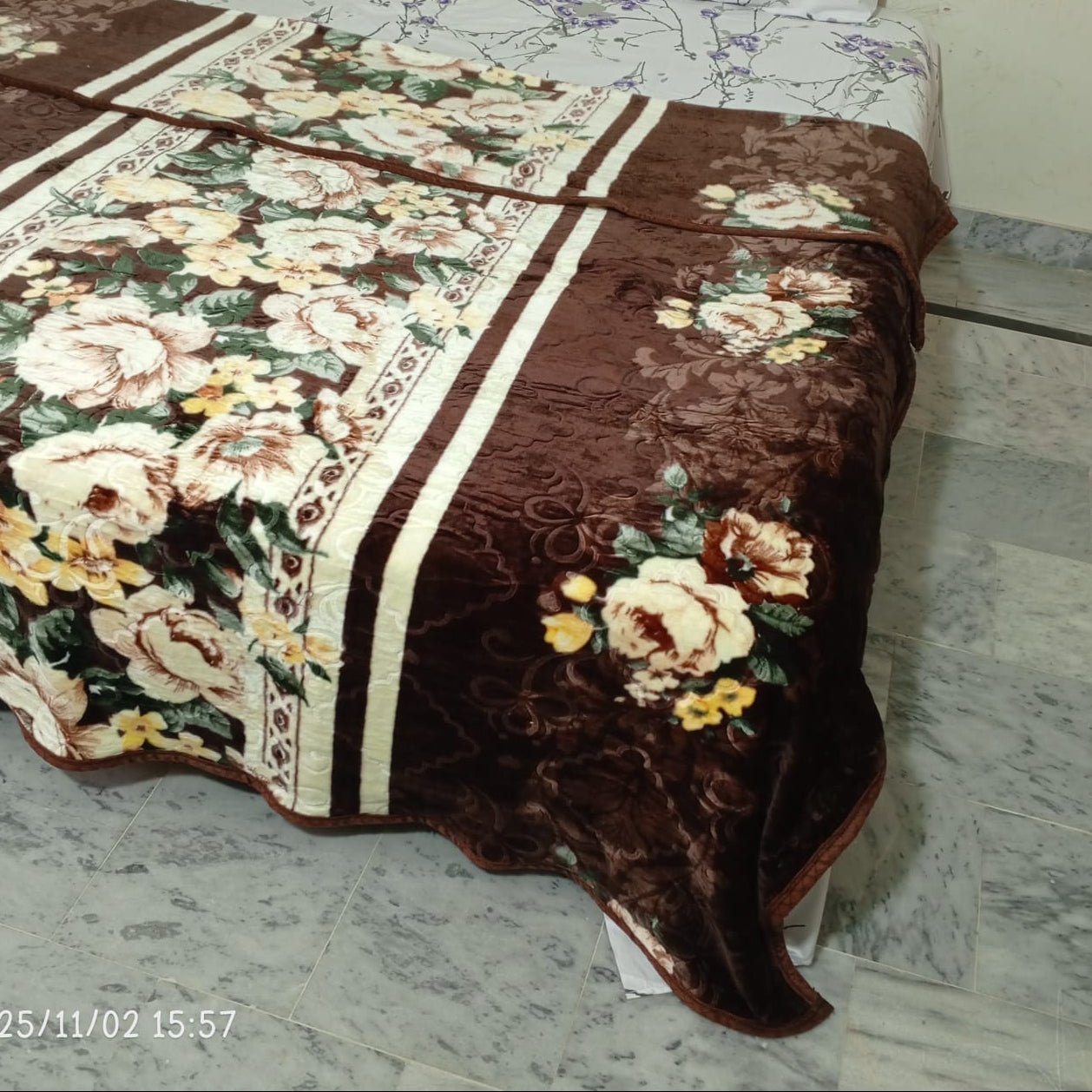 Brown floral blanket with cream and yellow flowers on a bed in a marble floor room