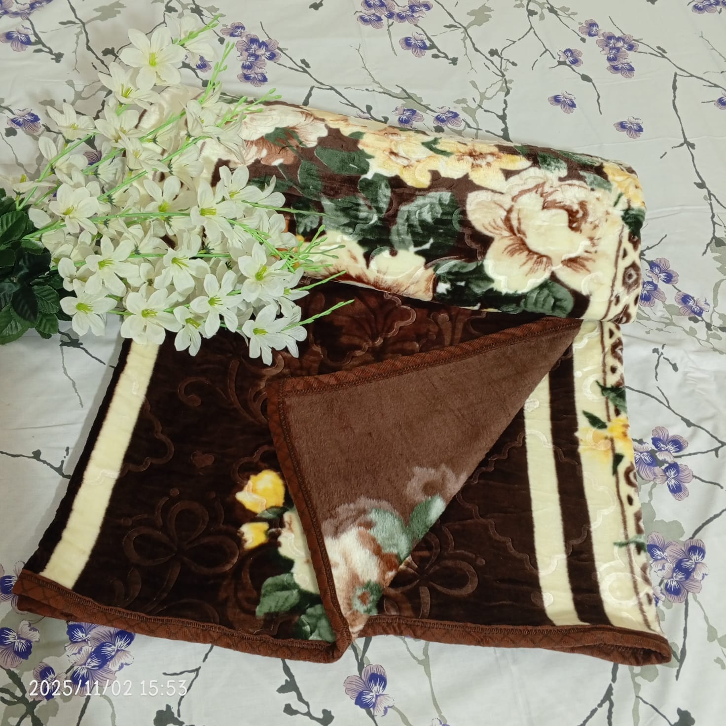 Brown floral fleece blanket with white artificial flowers on a floral bed sheet