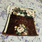Brown floral blanket with cream and yellow rose design on a white bed sheet with purple flowers