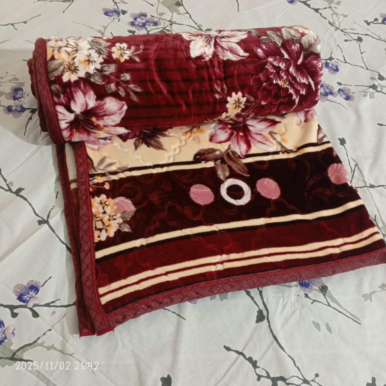 Rolled maroon floral blanket on a white floral bedsheet