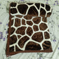 Brown and white giraffe print blanket on floral bedsheet, soft velvet texture.