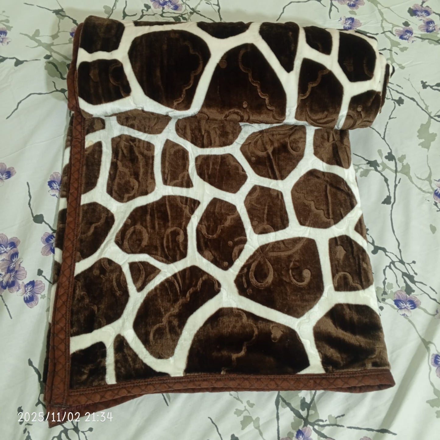 Brown and white giraffe print blanket on floral bedsheet, soft velvet texture.