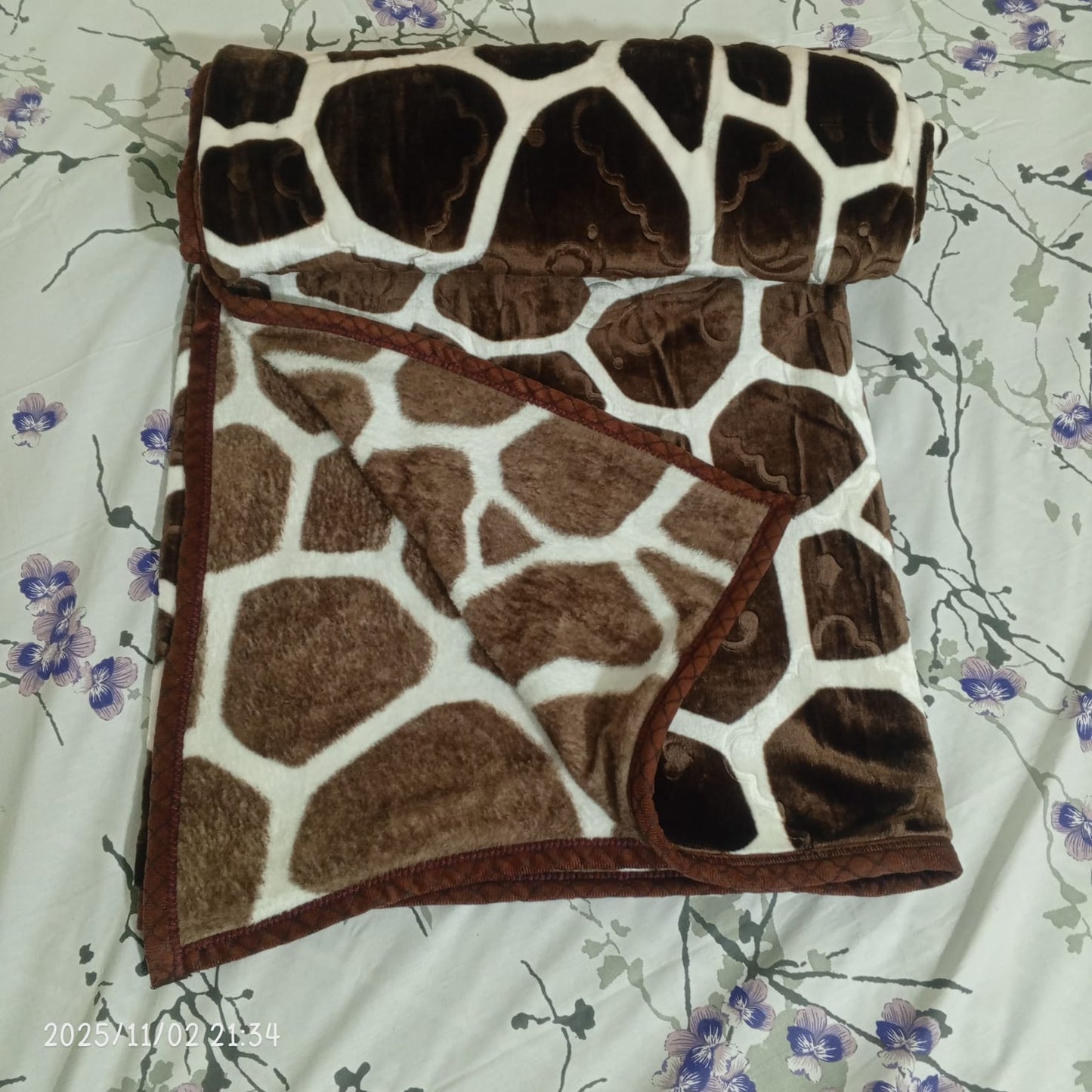 Folded giraffe print fleece blanket on a floral patterned bed sheet