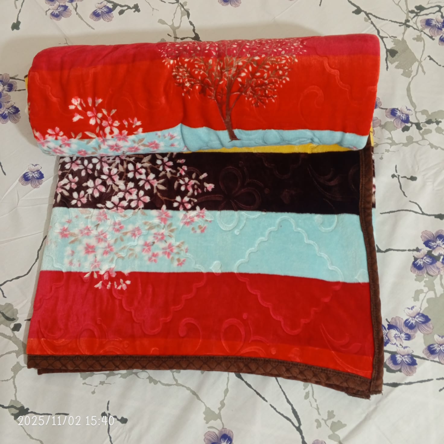 Colorful floral mink blanket folded on a white bed with purple flower print