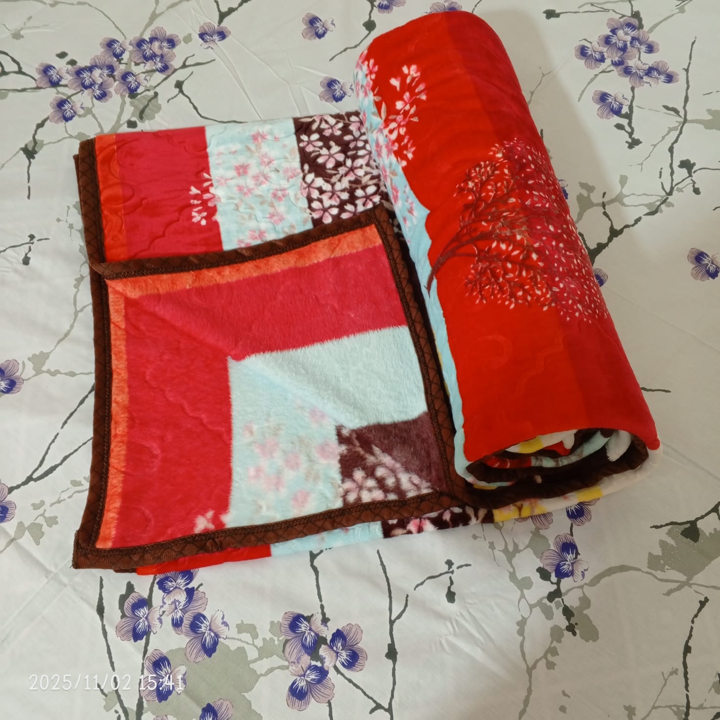 Red and brown floral blanket on white bed with purple flower pattern