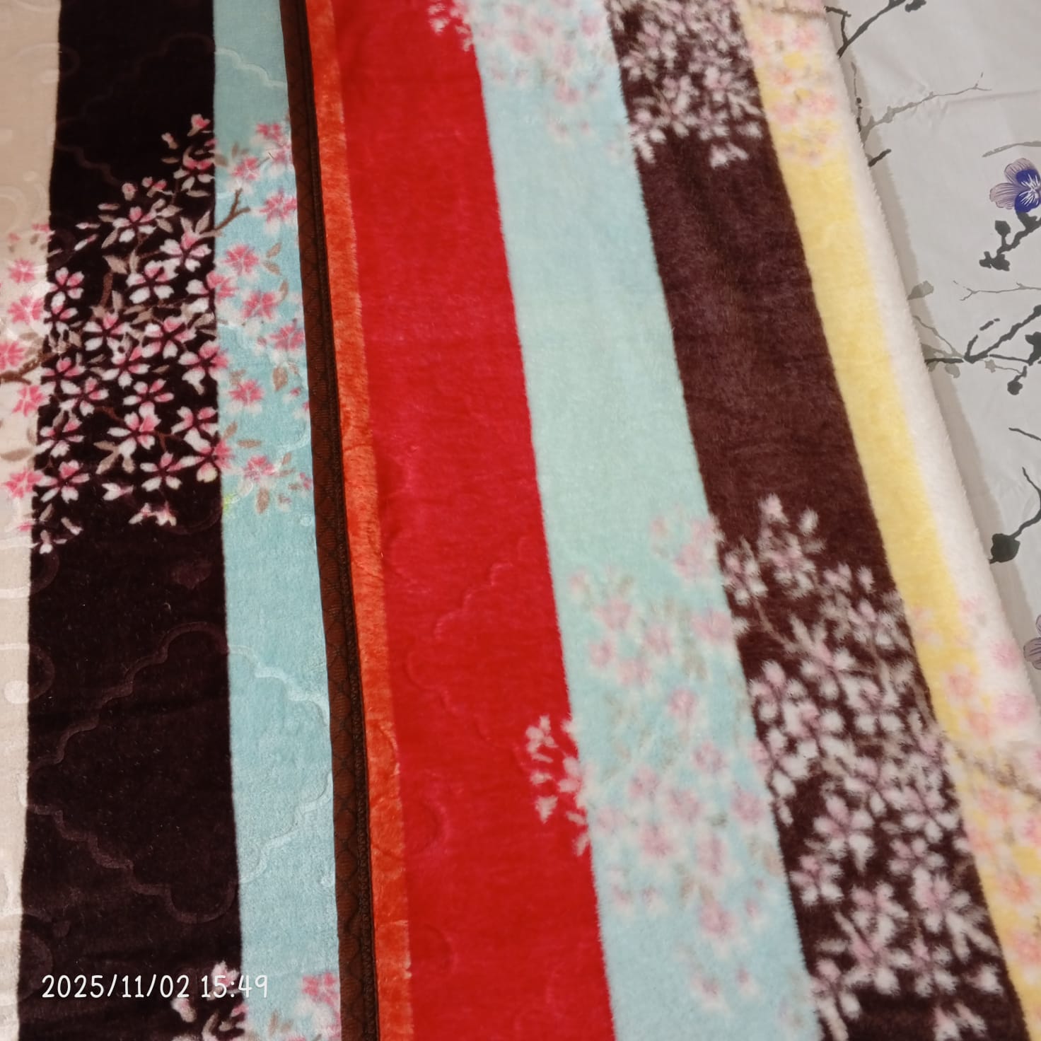 Striped floral blanket with red, brown, aqua, and yellow colors on a patterned bed